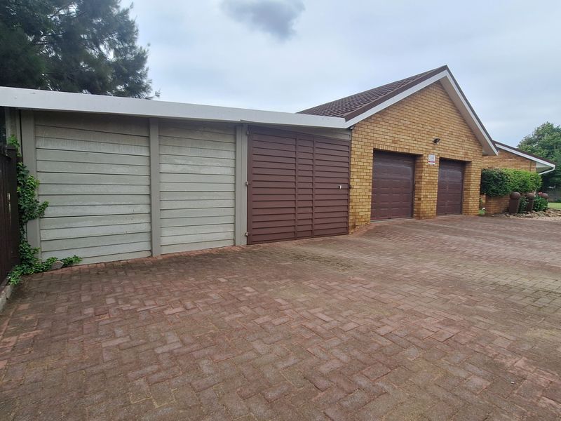 Exterior view of a property featuring a paved driveway, double garage doors, and additional storage or workshop space with precast walling.