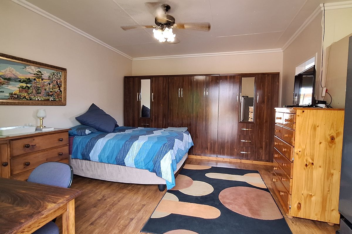 A spacious bedroom featuring extensive built-in wooden cupboards, a ceiling fan, and durable laminate flooring, offering a functional and well-maintained living space.