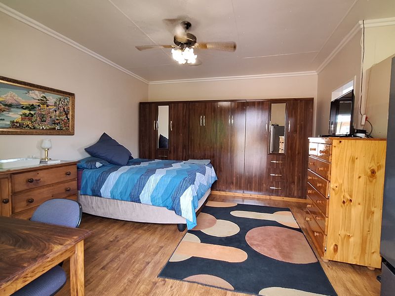 A spacious bedroom featuring extensive built-in wooden cupboards, a ceiling fan, and durable laminate flooring, offering a functional and well-maintained living space.