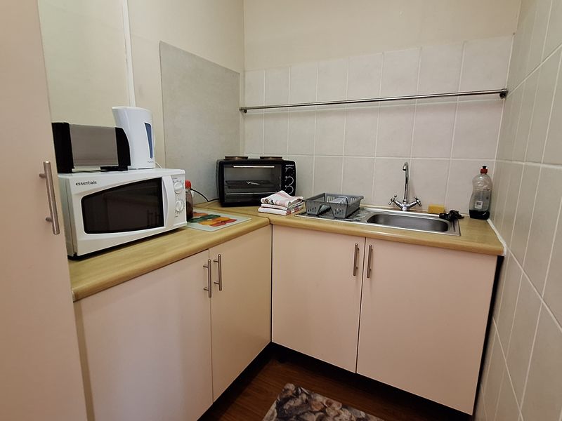 A compact scullery or kitchenette area featuring built-in cabinetry, a stainless steel sink, and tiled splashbacks, providing functional prep and wash-up space.