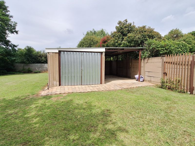 A rear garden view featuring a detached corrugated metal garage with an adjacent paved patio area, enclosed by precast concrete walls and timber fencing.