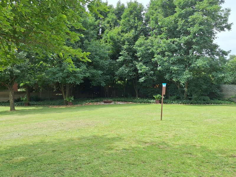 A spacious, well-maintained private garden featuring a large lawn area, mature trees, and a perimeter wall.