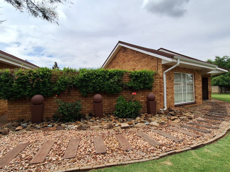 A well-maintained face brick house exterior featuring a landscaped garden, stone pathway, and a brick boundary wall with decorative features.