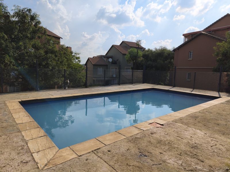 Communal swimming pool area featuring a paved deck and perimeter fencing, set within a residential apartment complex.