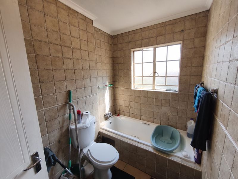 A compact bathroom featuring a built-in bathtub, toilet, and full-height ceramic wall tiling, offering a functional space with potential for modern updates.