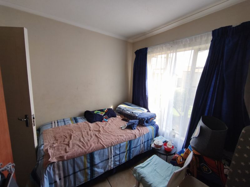 A compact bedroom featuring tiled flooring, neutral wall finishes, and a large window allowing natural light, suitable for a single bed setup.