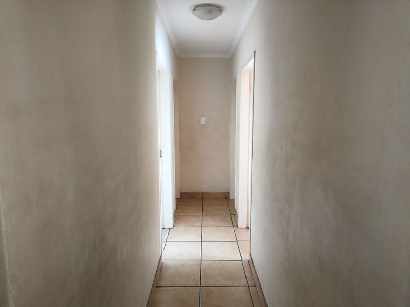 A narrow residential hallway featuring tiled flooring and a central ceiling light fixture, showing signs of wear on the wall surfaces.