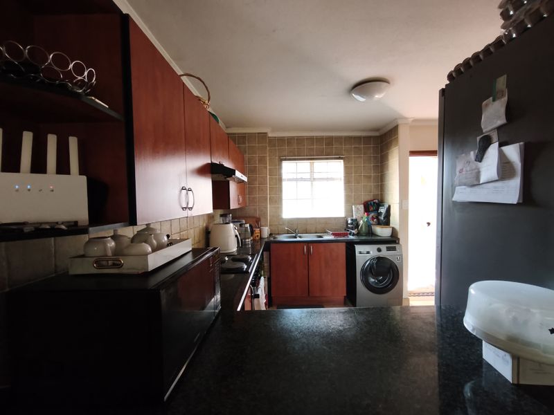 Functional kitchen featuring dark wood cabinetry, granite countertops, tiled backsplash, and an integrated washing machine with direct access to an exterior area.
