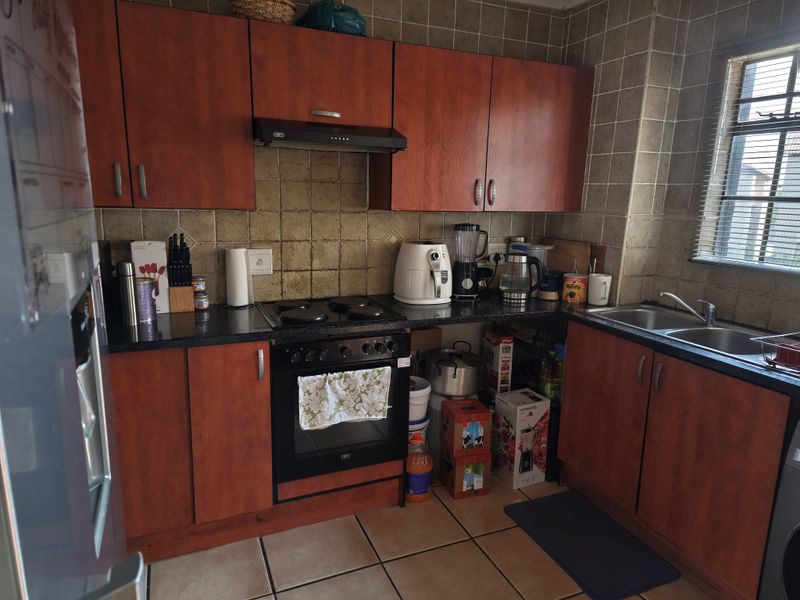 A functional kitchen featuring wood-tone cabinetry, dark countertops, a built-in oven with hob, and tiled finishes throughout.