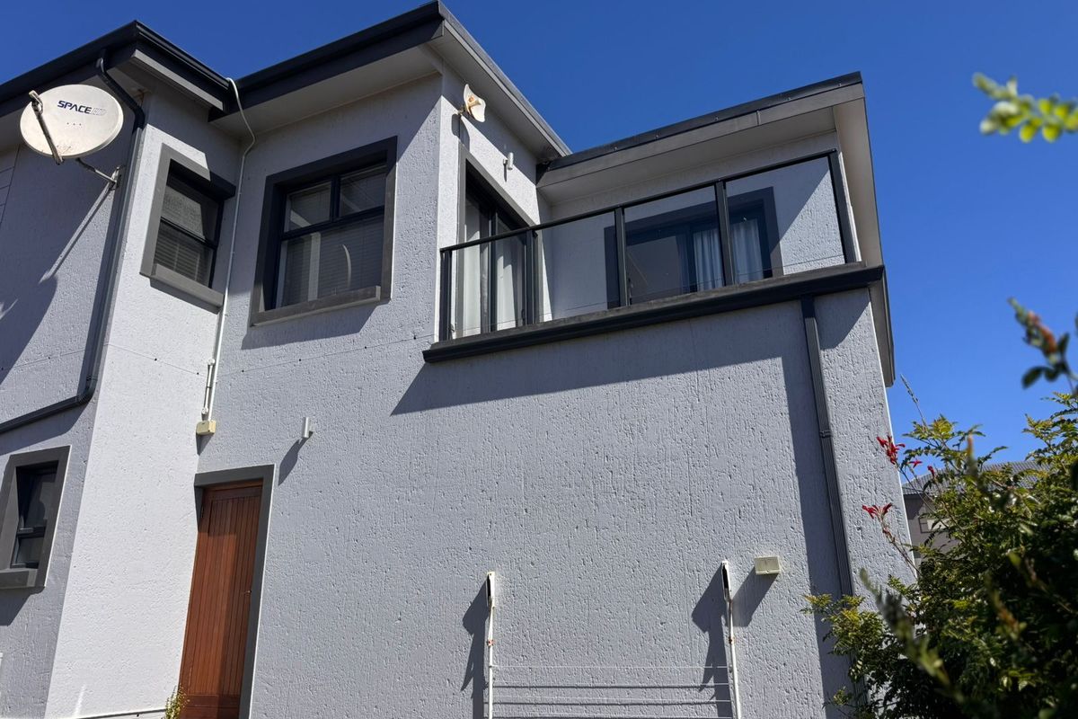 Rear elevation of a modern two-story house featuring a balcony with a glass balustrade and a textured render finish.