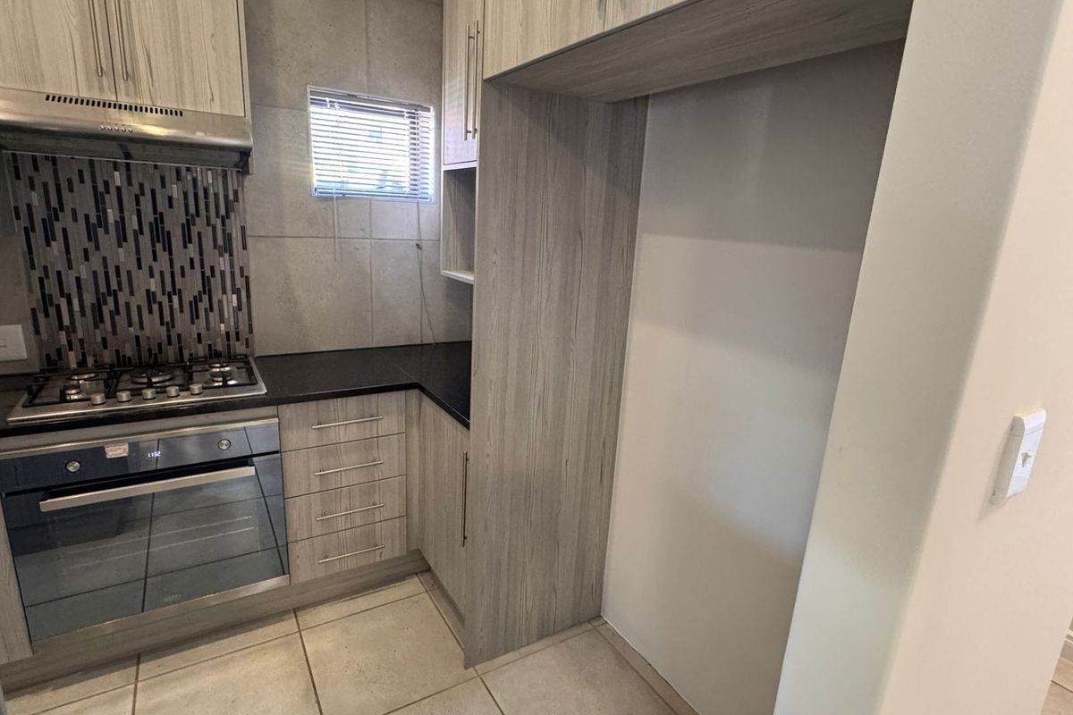 A modern kitchen featuring light wood-grain cabinetry, a gas hob with extractor, built-in oven, and a dedicated recess for a refrigerator.