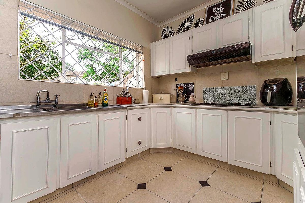 A functional kitchen featuring white cabinetry, tiled flooring, a built-in hob with extractor fan, and a large window with security bars.