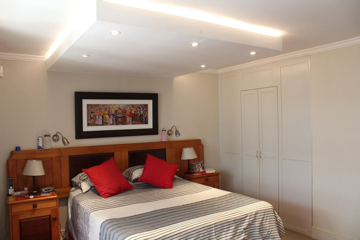 A well-maintained bedroom featuring a built-in wardrobe, recessed ceiling lighting, and decorative crown molding.