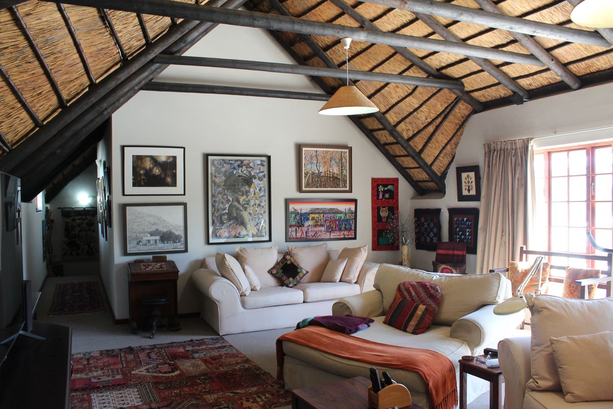 A cozy living room featuring a high vaulted ceiling with exposed timber rafters and traditional thatch roofing, creating a warm and rustic atmosphere.