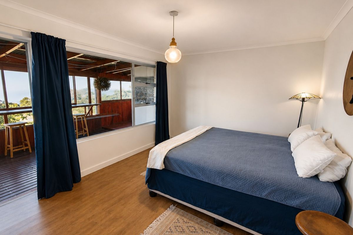 A bright bedroom featuring laminate flooring, a pendant light, and a large sliding glass door providing direct access to an outdoor deck area.