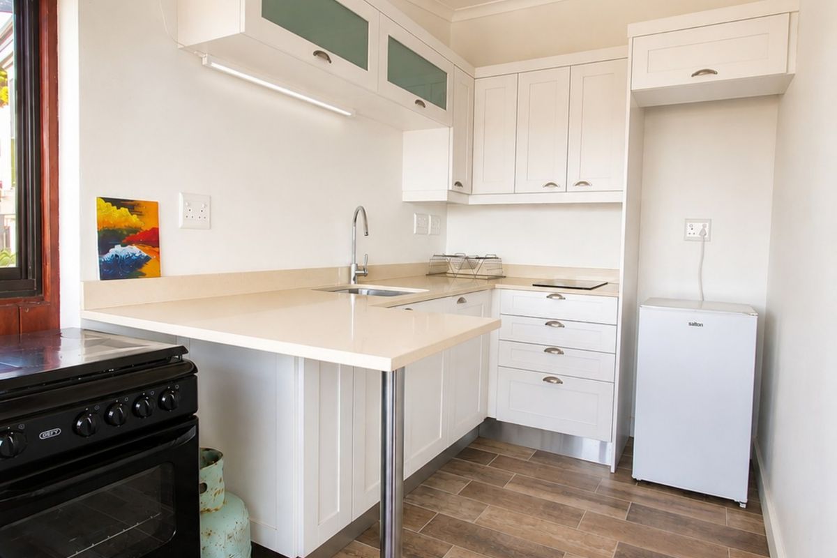 Compact kitchen featuring white cabinetry, stone countertops, stainless steel sink, and wood-look tiled flooring with an exposed timber beam overhead.