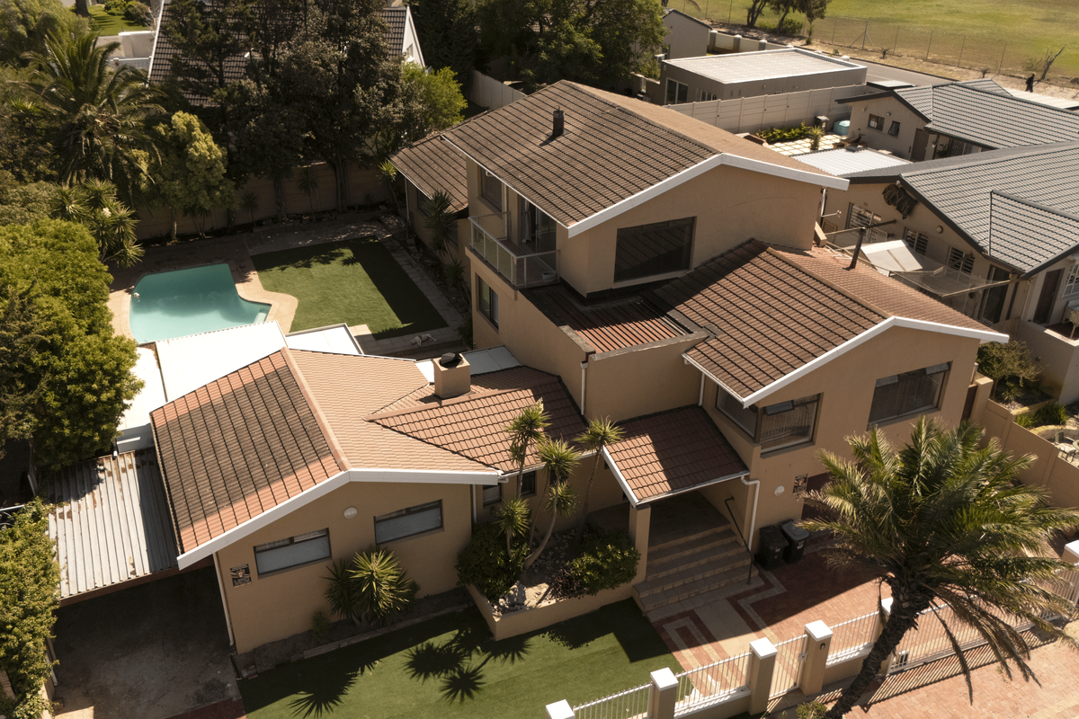 Aerial view of a multi-level residential property featuring a tiled roof, private swimming pool, landscaped garden, and paved driveway with carport.
