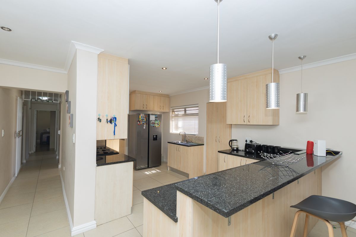 Modern kitchen featuring light wood cabinetry, granite countertops, a breakfast bar, and tiled flooring, with an open-plan layout leading to a hallway.