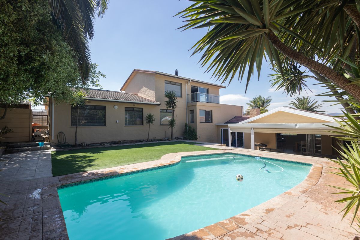 Rear view of the property featuring a swimming pool, artificial lawn, paved patio area, and a covered outdoor entertainment space.