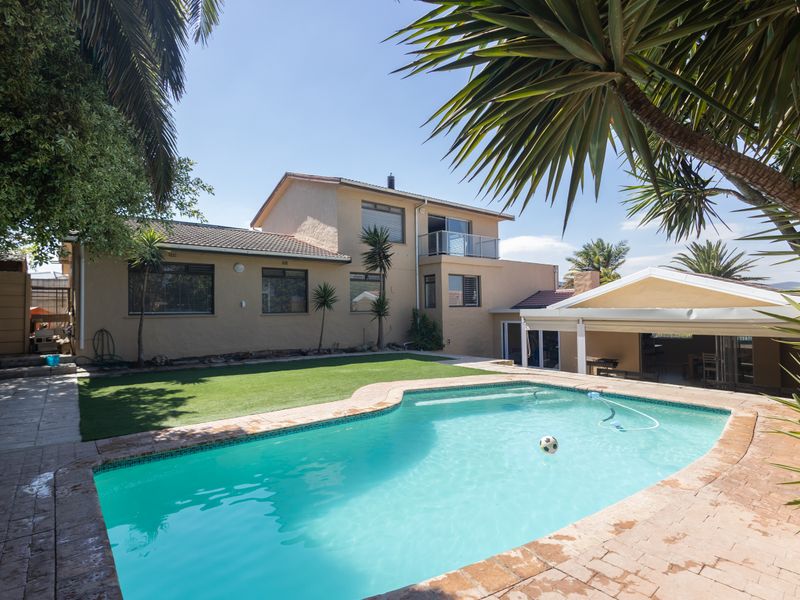 Rear view of the property featuring a swimming pool, artificial lawn, paved patio area, and a covered outdoor entertainment space.