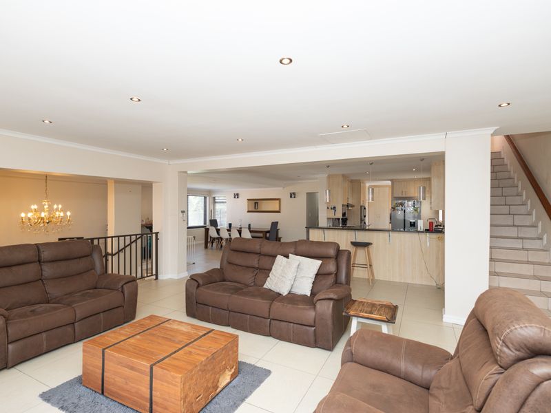 Spacious open-plan living area featuring tiled floors, recessed lighting, a functional kitchen with island, and an internal staircase leading to the upper level.