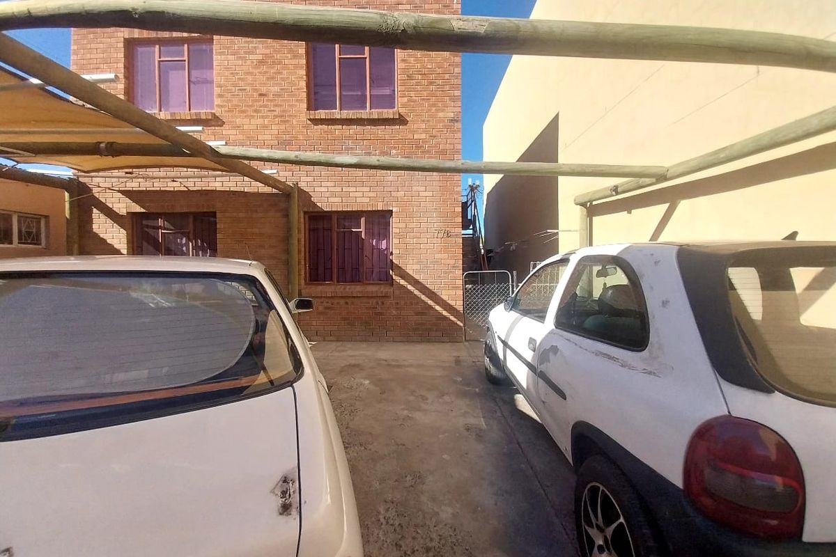 A view of the rear exterior brick facade featuring a timber pergola structure and concrete driveway area.