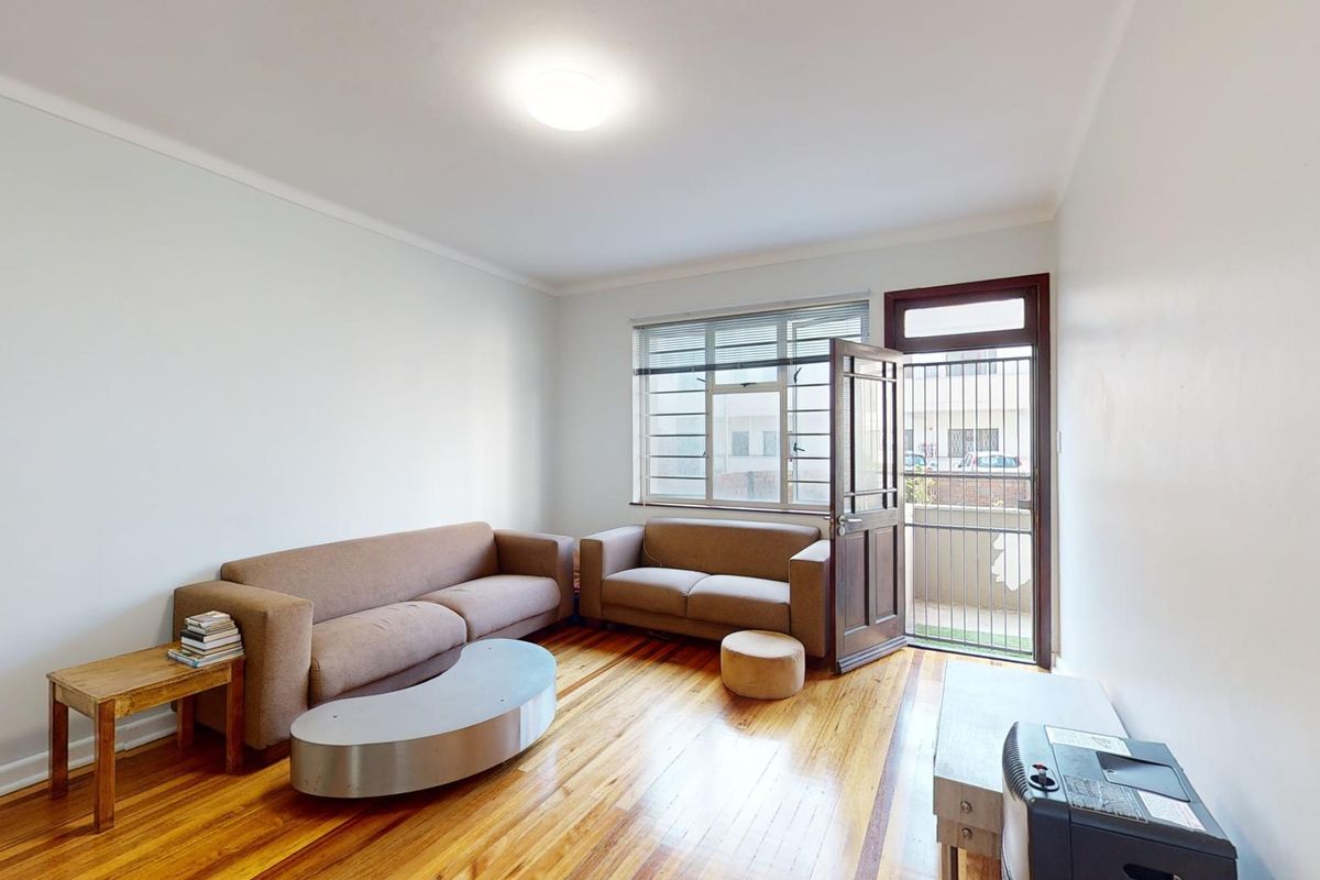 A living room featuring polished hardwood flooring, a security gate, and direct access to an outdoor area through a timber door.