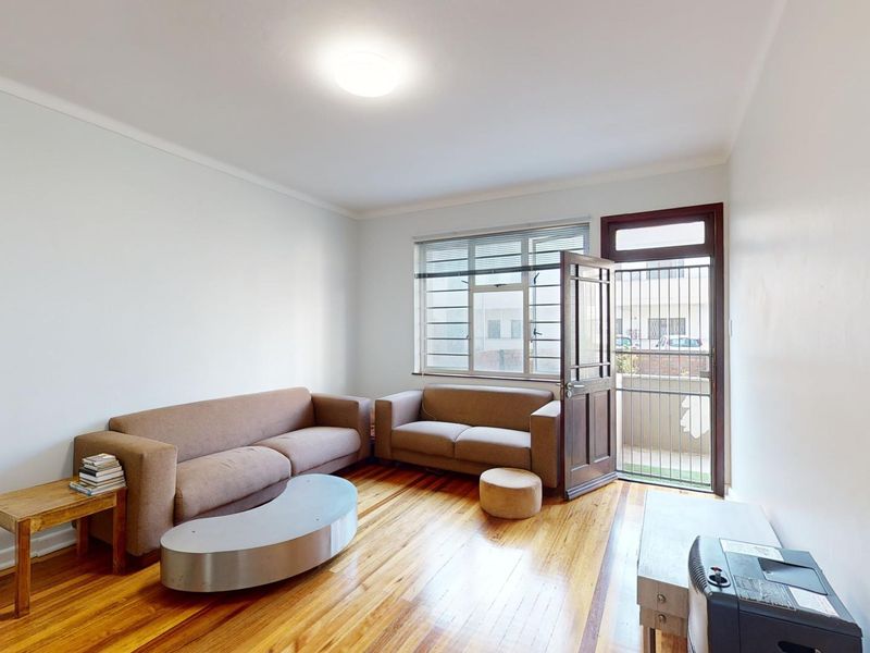 A living room featuring polished hardwood flooring, a security gate, and direct access to an outdoor area through a timber door.