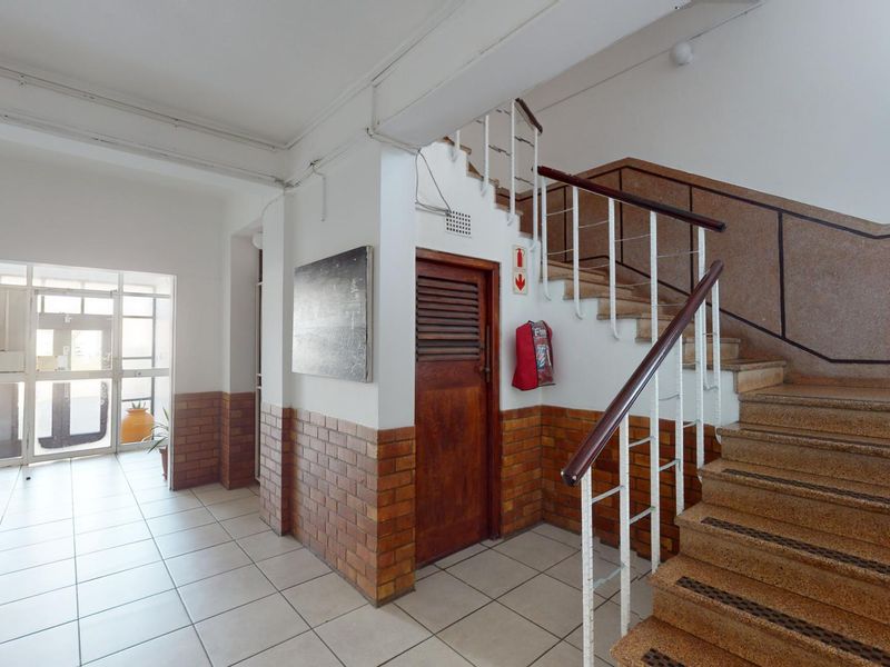 Communal apartment building entrance foyer featuring a staircase with metal handrails, brick wainscoting, and tiled flooring.
