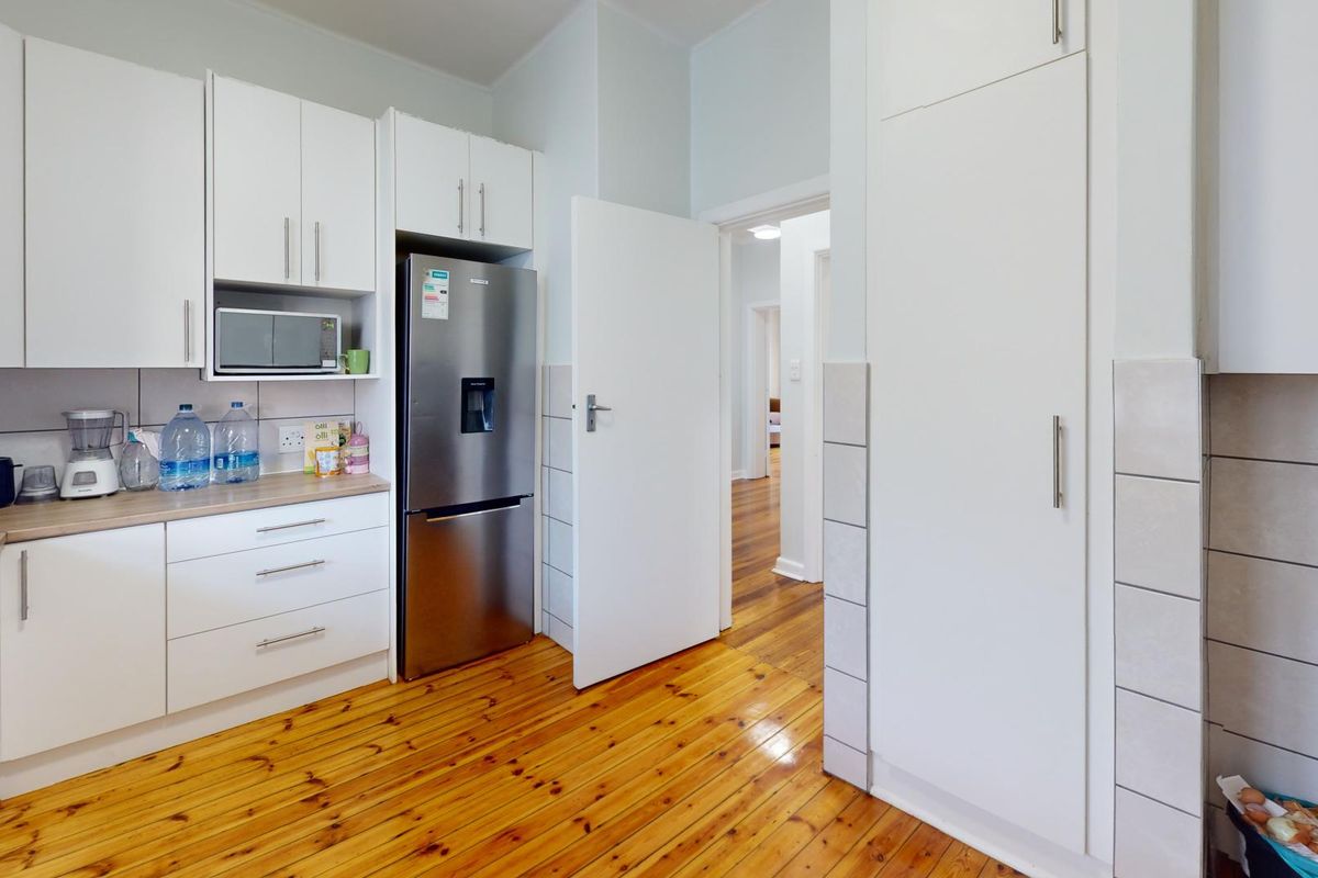 A functional kitchen featuring white cabinetry, laminate countertops, tiled backsplash, and warm timber flooring, with a seamless transition to the hallway.