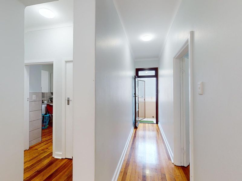A bright, clean hallway featuring polished hardwood flooring and access to adjacent rooms, leading towards an exterior security gate.