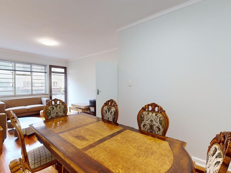Open-plan living and dining area featuring hardwood flooring, large windows with security bars, and access to an external security gate.