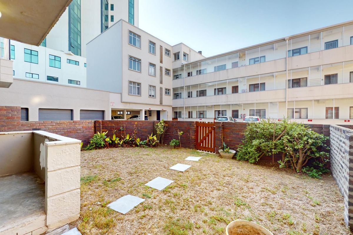 A private rear courtyard featuring a brick boundary wall, a small garden area with stepping stones, and a covered patio space.