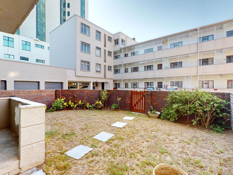 A private rear courtyard featuring a brick boundary wall, a small garden area with stepping stones, and a covered patio space.