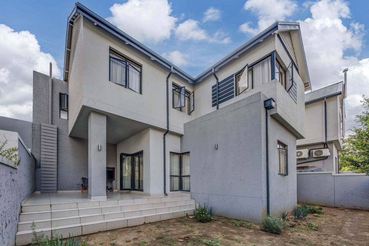 Rear view of a modern two-story house featuring a tiled patio, built-in outdoor braai, and clean architectural lines with grey and white exterior finishes.