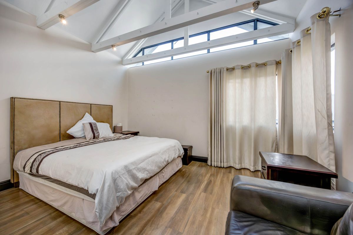 Spacious bedroom featuring high vaulted ceilings with exposed beams, clerestory windows, and durable wood-look flooring.