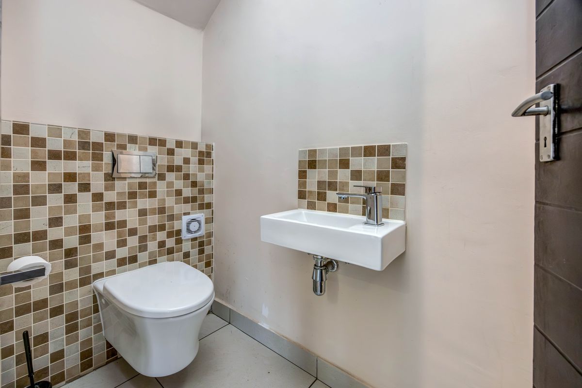 A compact guest bathroom featuring a wall-mounted toilet, a modern floating basin with chrome fixtures, and decorative mosaic tile accents.