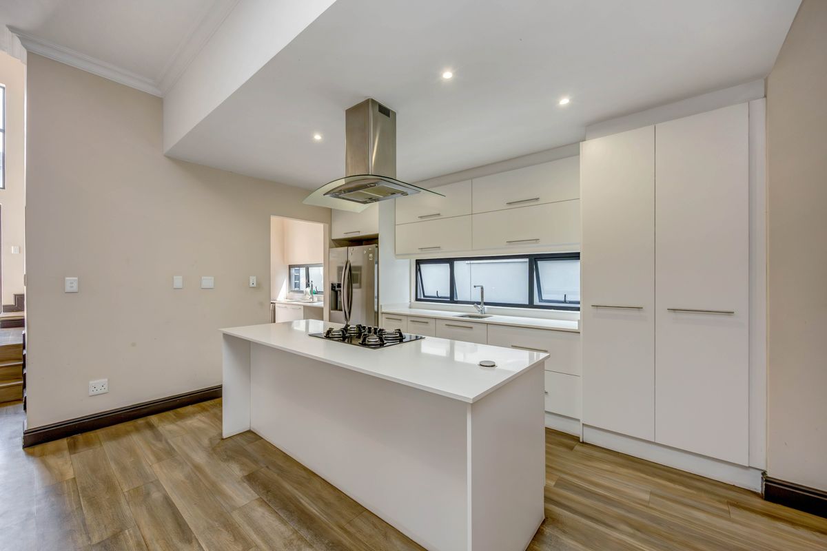 Modern kitchen featuring a central island with a built-in gas hob, stainless steel extractor fan, sleek white cabinetry, and wood-look flooring.