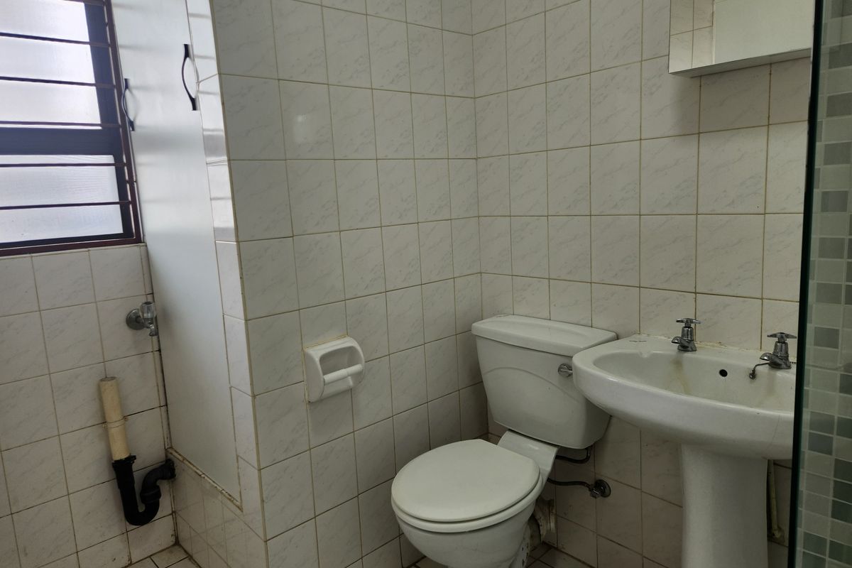 A dated bathroom featuring a pedestal basin, standard toilet, and full-height wall tiling with an adjacent window.