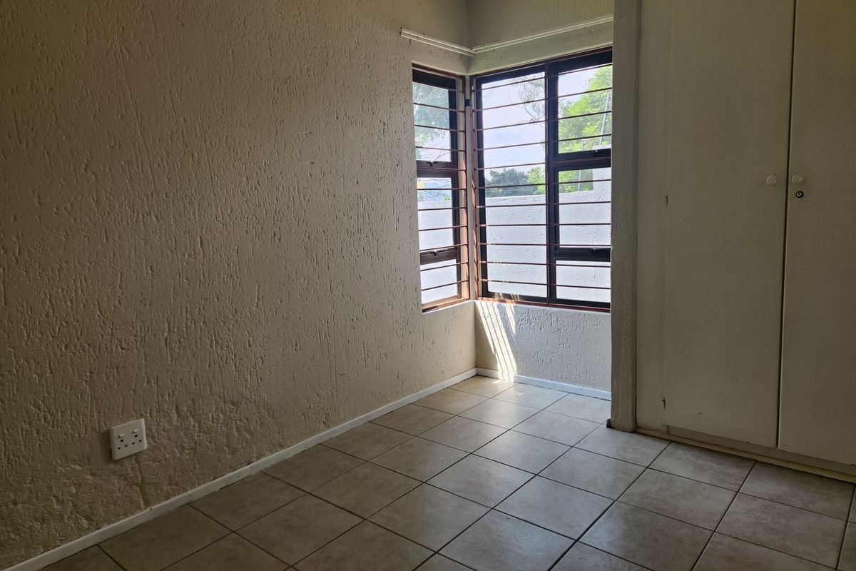 A vacant bedroom featuring tiled flooring, built-in cupboards, and corner windows with security bars.