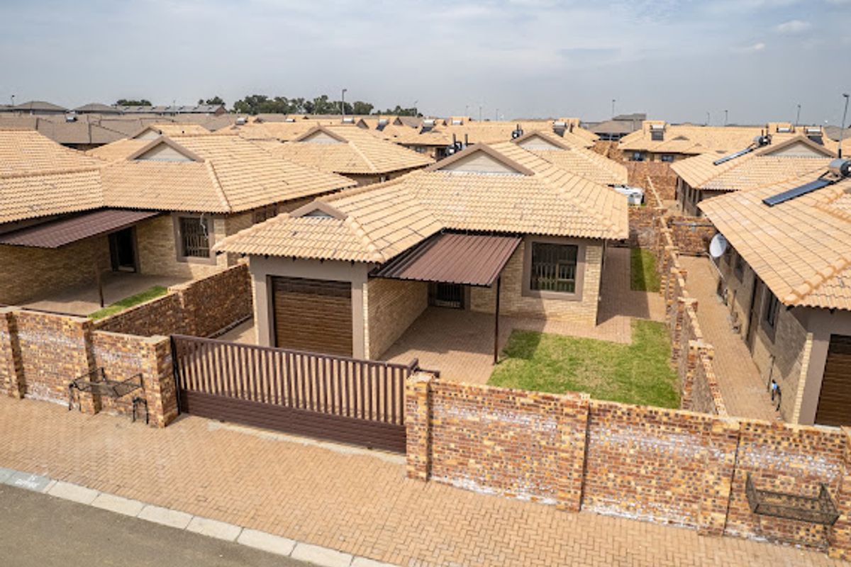 Aerial view of a residential property featuring a tiled roof, brick perimeter wall, paved driveway, and a single garage.