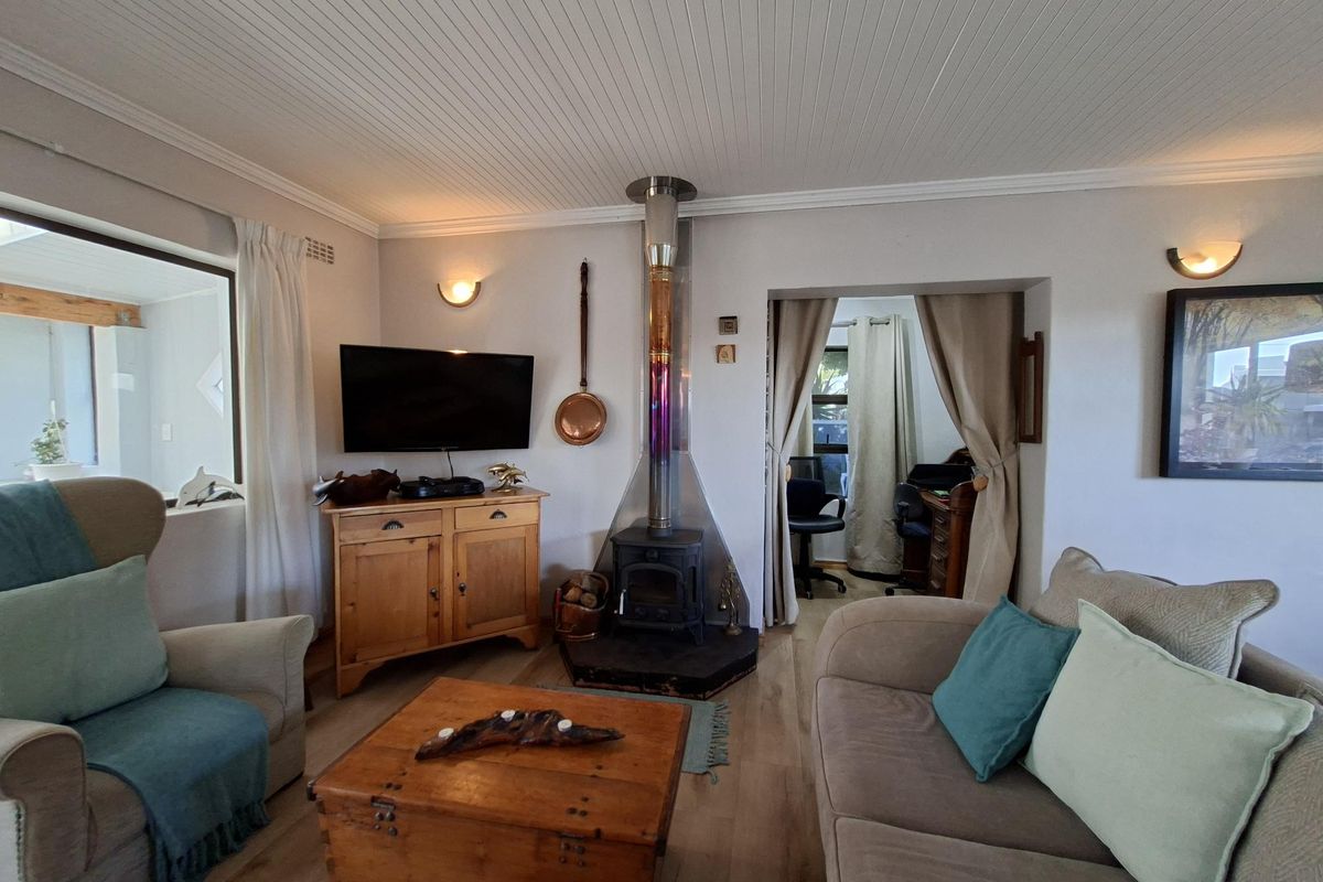 A cozy living room featuring a central wood-burning stove with a stainless steel flue, beadboard ceiling, and warm laminate flooring.