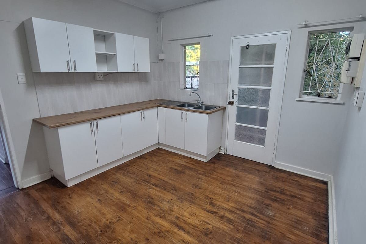 A functional kitchen space featuring white cabinetry, wooden countertops, a stainless steel sink, and original timber flooring, offering a blank canvas for updates.