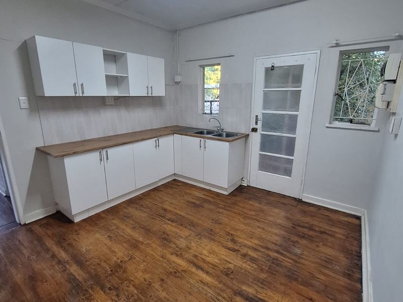 A functional kitchen space featuring white cabinetry, wooden countertops, a stainless steel sink, and original timber flooring, offering a blank canvas for updates.
