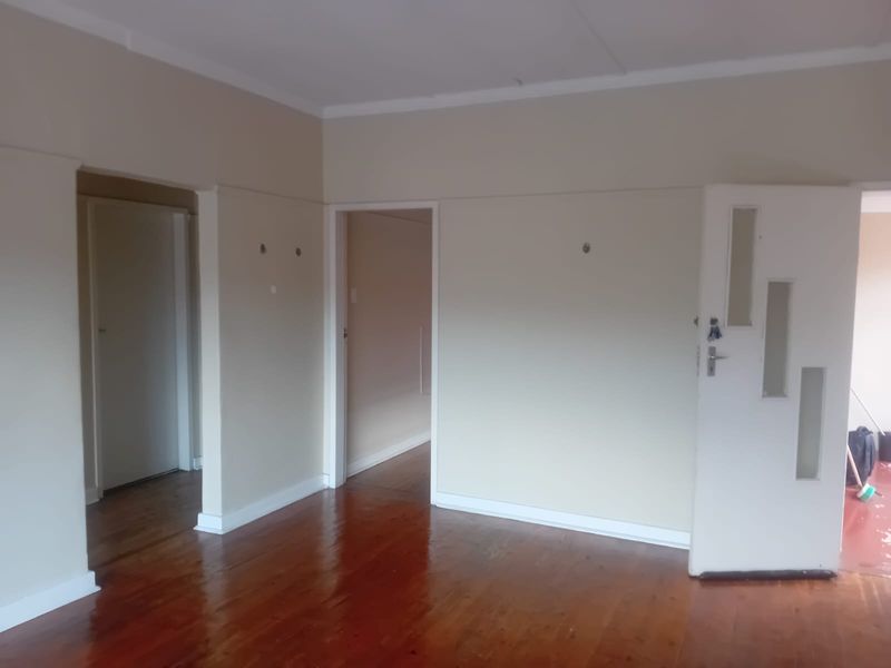 An empty living area featuring polished hardwood flooring, neutral wall tones, and multiple internal doorways leading to adjacent rooms.