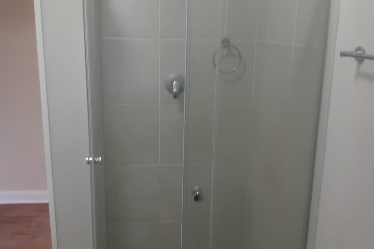 A functional bathroom shower area featuring a glass enclosure, tiled walls, and a distinctive black and white mosaic tiled floor.