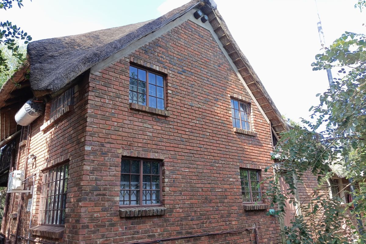 A side view of a traditional double-story house featuring exposed brickwork, timber-framed windows, and a classic thatched roof.