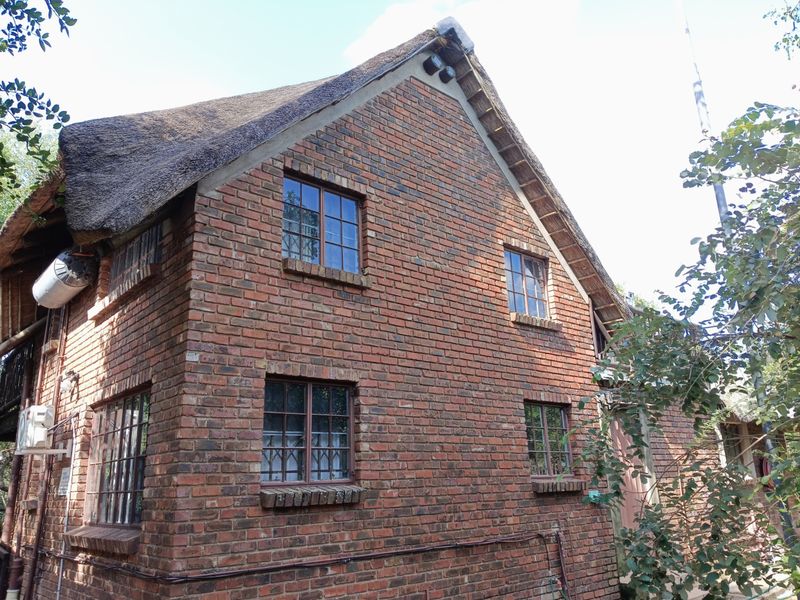 A side view of a traditional double-story house featuring exposed brickwork, timber-framed windows, and a classic thatched roof.