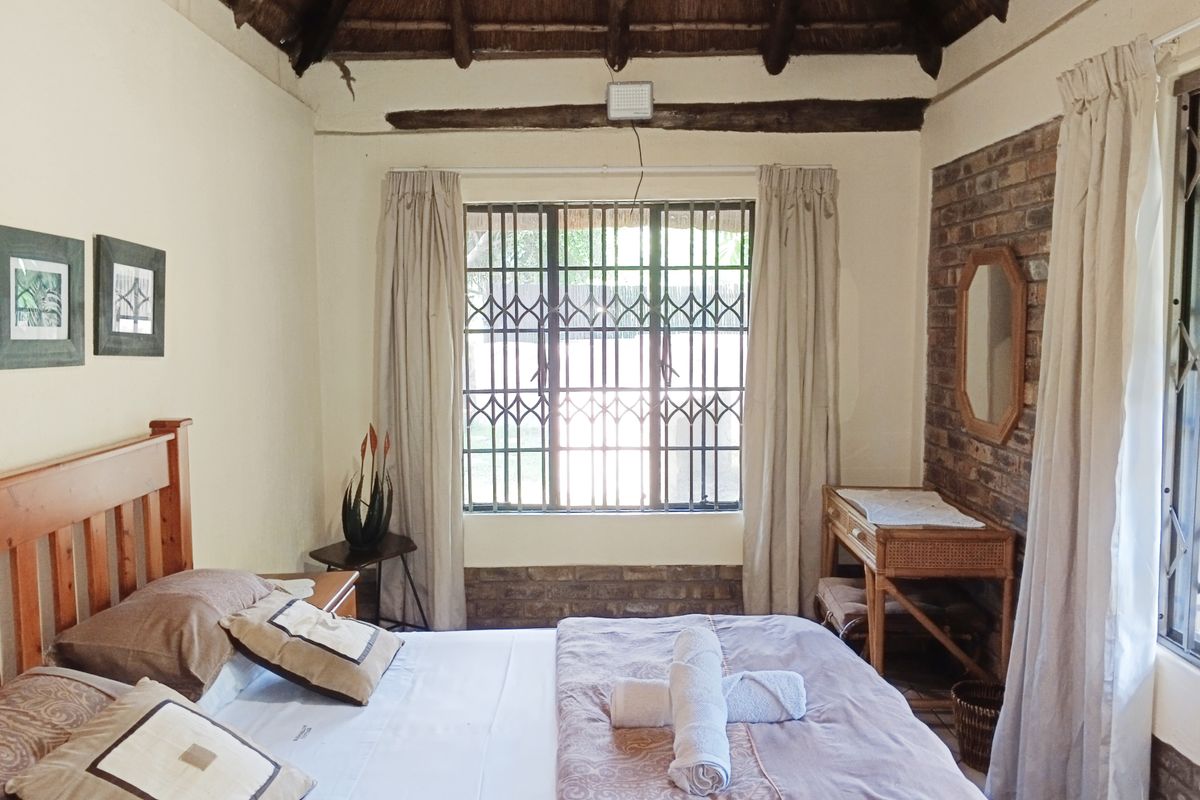 A cozy bedroom featuring a traditional thatched roof with exposed timber beams and a rustic exposed brick feature wall.