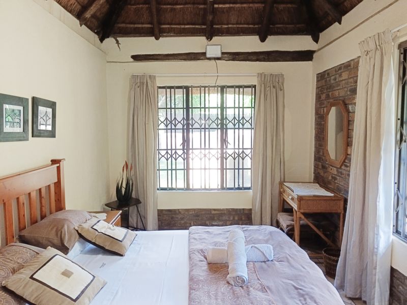 A cozy bedroom featuring a traditional thatched roof with exposed timber beams and a rustic exposed brick feature wall.